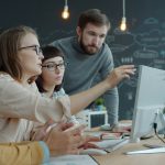 Colleagues gathered at a desk pointing at a computer screen while discussing a project